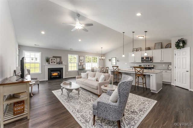 living room with ceiling fan with notable chandelier, dark wood-type flooring, and vaulted ceiling