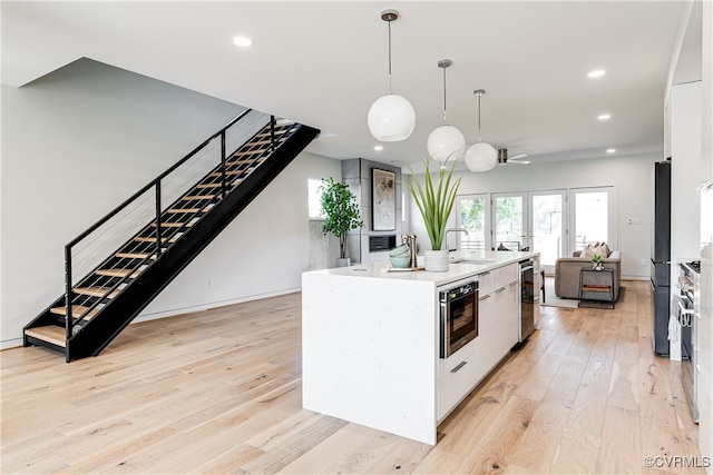 kitchen with an island with sink, decorative light fixtures, white cabinetry, stainless steel appliances, and light hardwood / wood-style floors