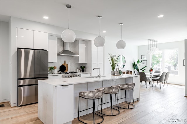 kitchen featuring a center island with sink, decorative light fixtures, stainless steel fridge, and white cabinetry