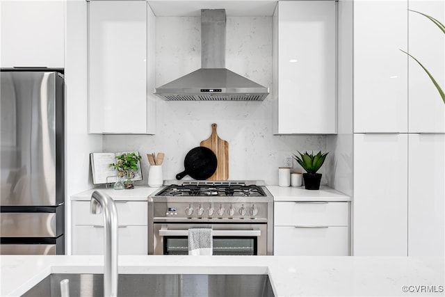 kitchen featuring light stone counters, white cabinets, appliances with stainless steel finishes, and wall chimney exhaust hood