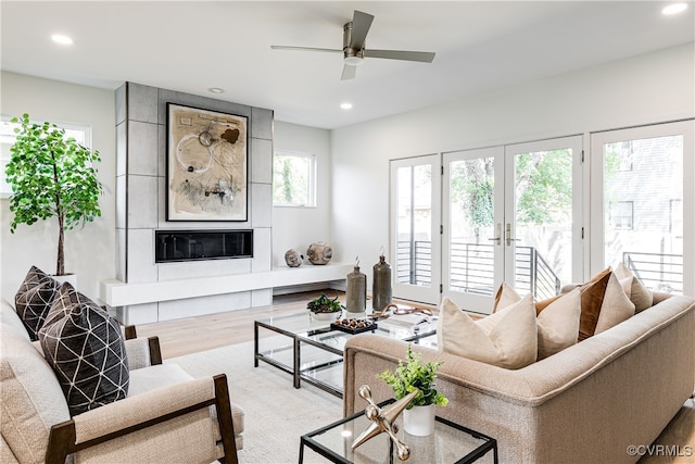 living room featuring a healthy amount of sunlight, light hardwood / wood-style floors, a large fireplace, and ceiling fan