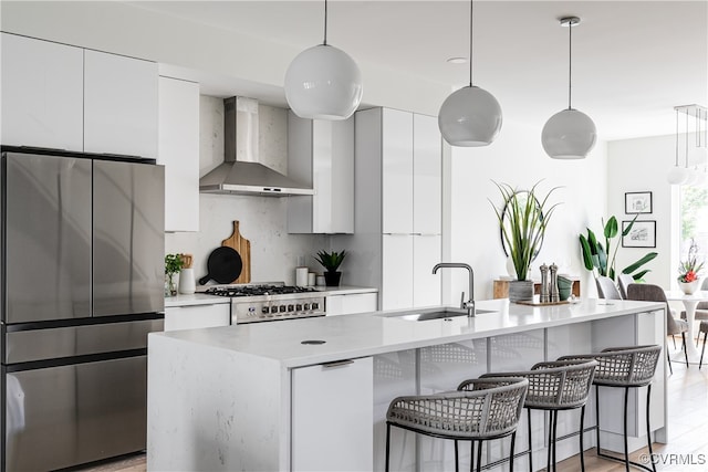 kitchen with decorative light fixtures, stainless steel appliances, sink, and wall chimney range hood