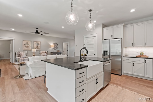 kitchen with white cabinets, light hardwood / wood-style flooring, stainless steel appliances, a center island with sink, and ceiling fan