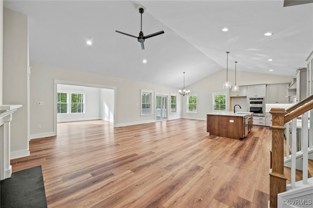 unfurnished living room featuring light wood-type flooring, sink, a fireplace, ceiling fan with notable chandelier, and vaulted ceiling