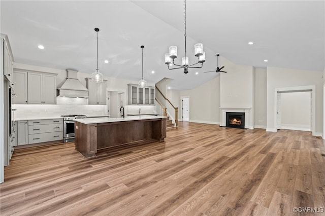 kitchen featuring an island with sink, custom exhaust hood, hanging light fixtures, high end range, and vaulted ceiling