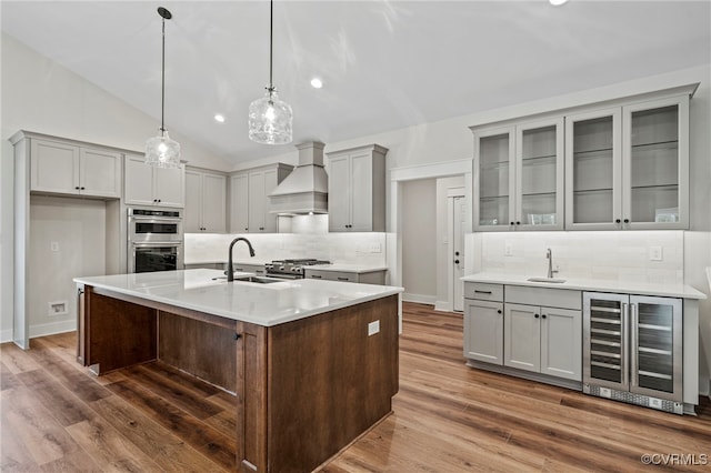 kitchen featuring vaulted ceiling, stainless steel appliances, custom exhaust hood, a kitchen island with sink, and sink