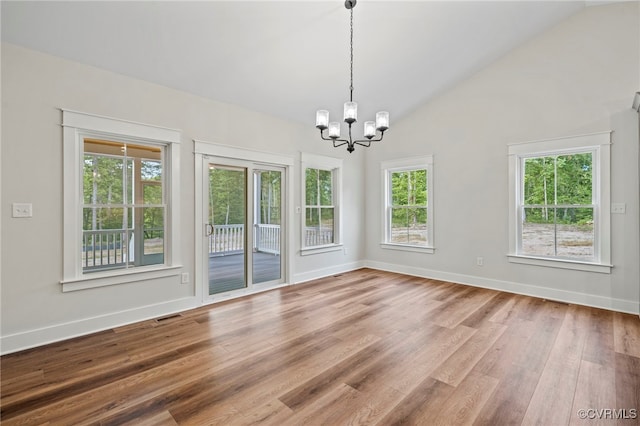 empty room featuring hardwood / wood-style flooring, lofted ceiling, plenty of natural light, and a notable chandelier