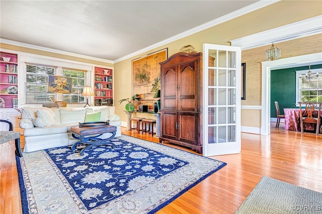 living room featuring crown molding, built in shelves, an inviting chandelier, and light hardwood / wood-style flooring