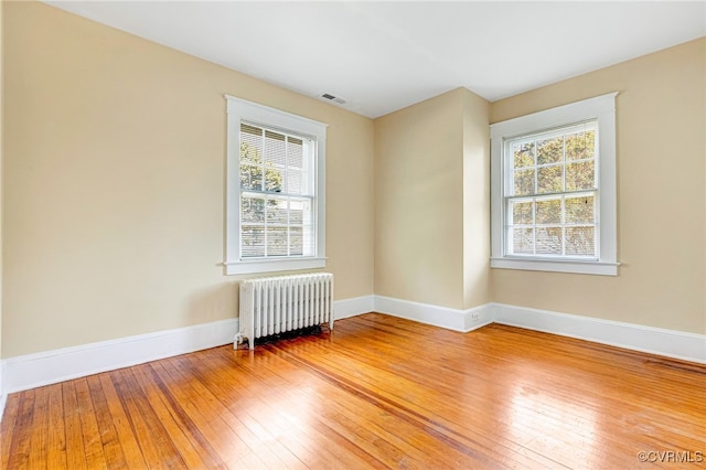 unfurnished room featuring radiator heating unit, a wealth of natural light, and hardwood / wood-style floors