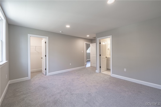 unfurnished bedroom with light colored carpet, a closet, ensuite bathroom, and a walk in closet