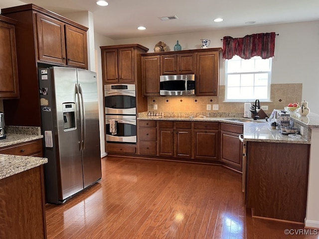 kitchen featuring sink, tasteful backsplash, dark wood-type flooring, appliances with stainless steel finishes, and light stone countertops