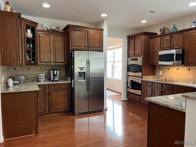 kitchen with appliances with stainless steel finishes, dark wood-type flooring, light stone counters, and tasteful backsplash