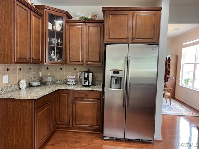 kitchen featuring stainless steel refrigerator with ice dispenser, light stone counters, hardwood / wood-style flooring, and backsplash