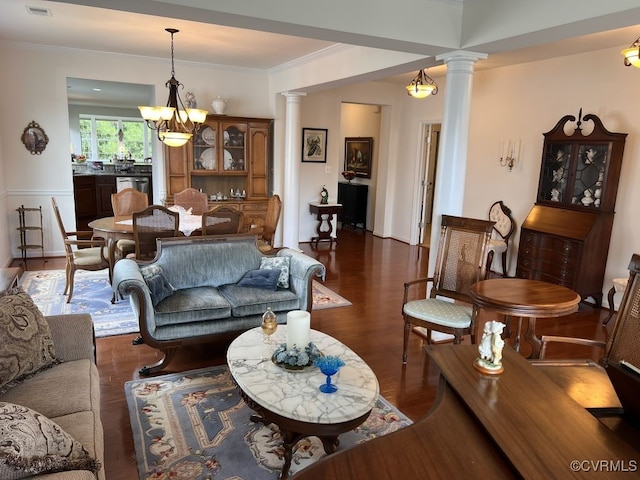 living room with a notable chandelier, ornamental molding, dark wood-type flooring, and ornate columns