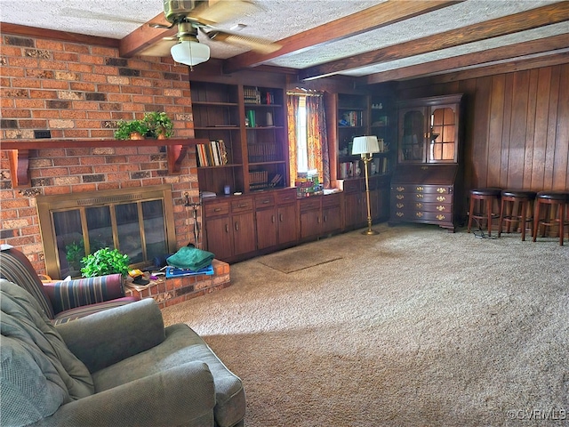 living room with a textured ceiling, beam ceiling, a brick fireplace, carpet, and ceiling fan