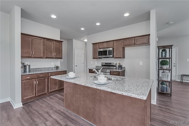 kitchen with stainless steel appliances, dark wood-style floors, an island with sink, and light stone countertops