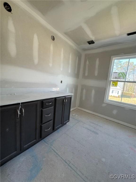 kitchen featuring baseboards, light countertops, and dark cabinetry