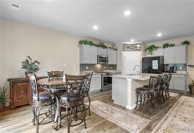 kitchen with a kitchen bar, a center island with sink, appliances with stainless steel finishes, and light hardwood / wood-style floors