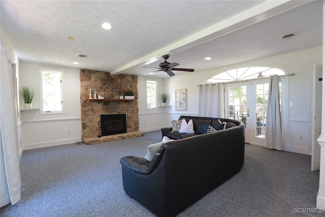 carpeted living room with french doors, a textured ceiling, ceiling fan, beam ceiling, and a stone fireplace