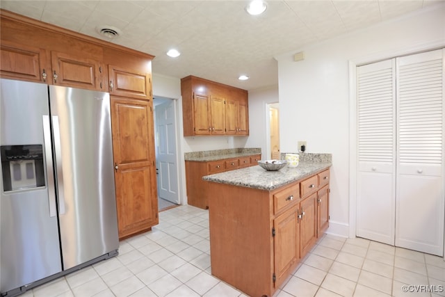 kitchen with stainless steel fridge, light stone countertops, and light tile patterned floors