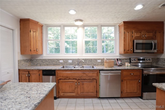 kitchen with light stone countertops, sink, light tile patterned floors, and stainless steel appliances