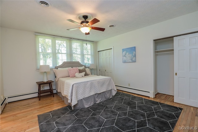 bedroom featuring ceiling fan, a textured ceiling, a baseboard radiator, wood-type flooring, and multiple closets