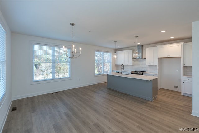 kitchen with white cabinets, a healthy amount of sunlight, wall chimney range hood, and an island with sink