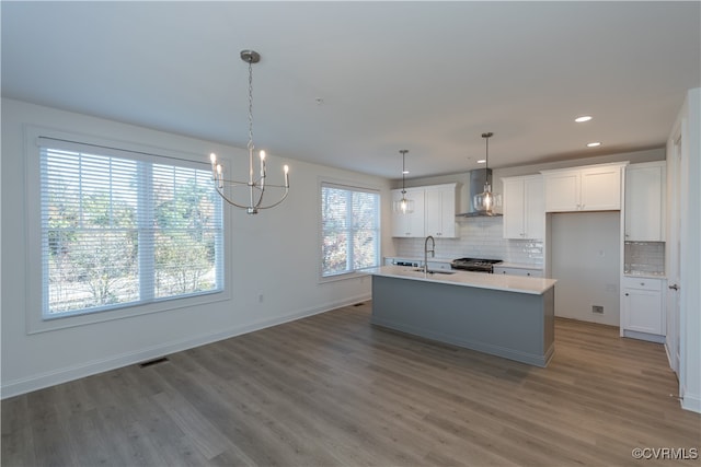 kitchen with hardwood / wood-style flooring, white cabinetry, wall chimney range hood, and a kitchen island with sink