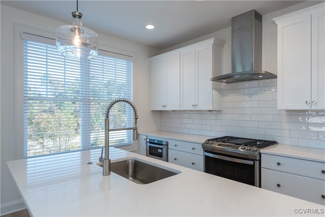 kitchen with white cabinetry, stainless steel range, wall chimney range hood, and sink