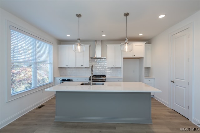 kitchen featuring a center island with sink, a healthy amount of sunlight, and wall chimney range hood