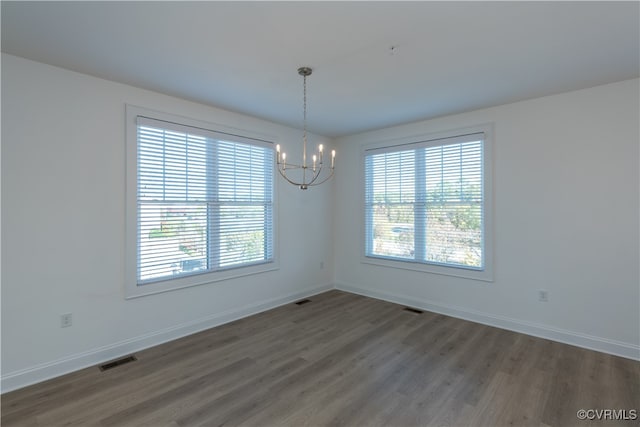 spare room with a notable chandelier, plenty of natural light, and dark hardwood / wood-style floors