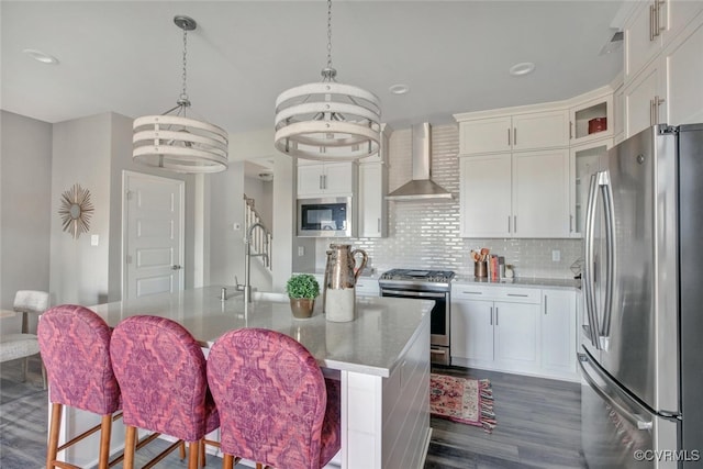 kitchen with wall chimney exhaust hood, stainless steel appliances, a center island with sink, a chandelier, and white cabinetry