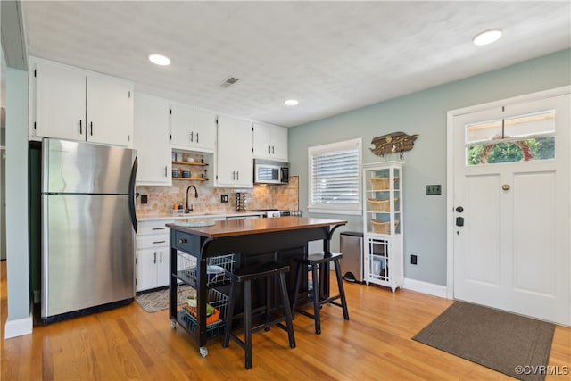 kitchen with light hardwood / wood-style flooring, decorative backsplash, white cabinetry, and appliances with stainless steel finishes