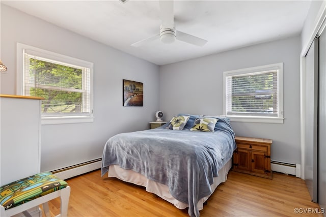 bedroom with a baseboard radiator, light hardwood / wood-style floors, and multiple windows