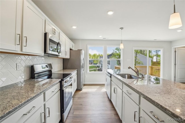 kitchen featuring light stone counters, a sink, stainless steel appliances, backsplash, and dark wood-style floors