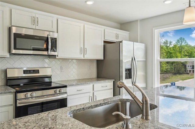 kitchen with white cabinets, a sink, tasteful backsplash, light stone countertops, and appliances with stainless steel finishes