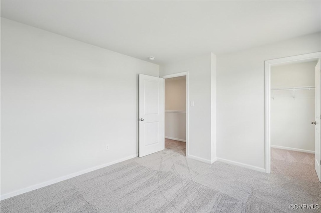 unfurnished bedroom with a spacious closet, carpet flooring, and baseboards