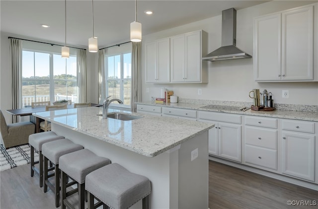 kitchen featuring stovetop, sink, wall chimney range hood, and an island with sink