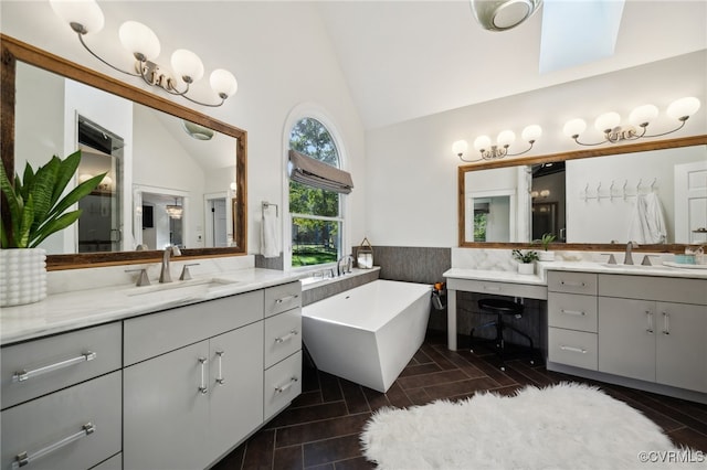 bathroom with vanity, vaulted ceiling with skylight, and a tub