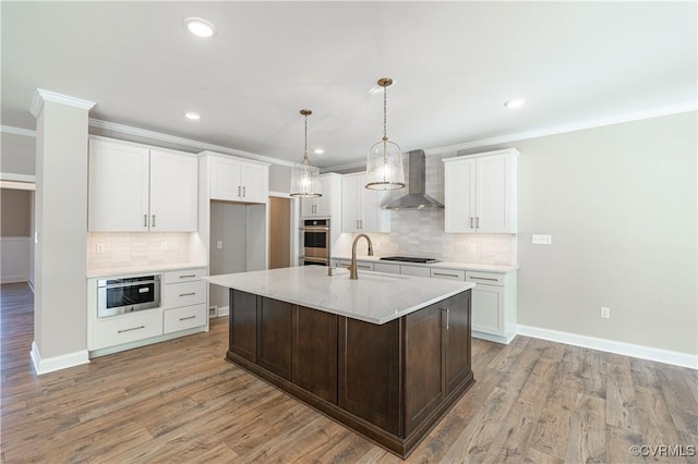 kitchen featuring wall chimney exhaust hood, light hardwood / wood-style flooring, a center island with sink, oven, and white cabinets