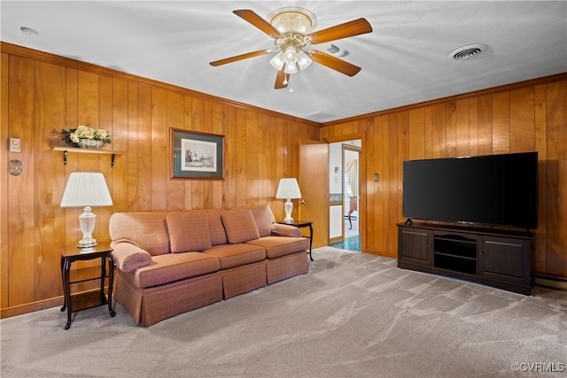 living room with ceiling fan, wood walls, light carpet, and crown molding