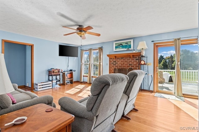 living room with light hardwood / wood-style floors, a textured ceiling, a fireplace, and ceiling fan