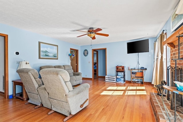 living room featuring a brick fireplace, a textured ceiling, hardwood / wood-style flooring, and ceiling fan