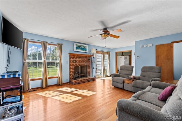 living room featuring ceiling fan, a textured ceiling, light hardwood / wood-style flooring, and a fireplace