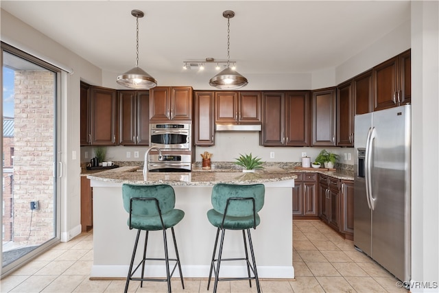 kitchen featuring light stone counters, plenty of natural light, stainless steel appliances, and a center island with sink