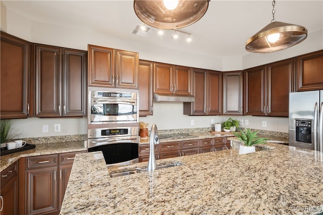 kitchen featuring decorative light fixtures, light stone counters, sink, and appliances with stainless steel finishes