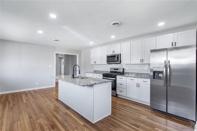 kitchen with appliances with stainless steel finishes, white cabinetry, sink, light stone countertops, and a center island with sink