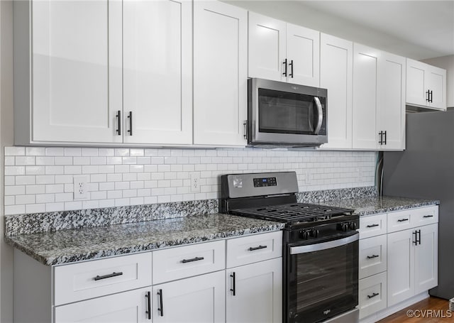 kitchen with white cabinetry, appliances with stainless steel finishes, backsplash, and dark stone counters