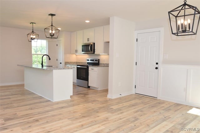 kitchen with decorative light fixtures, a center island with sink, stainless steel appliances, and white cabinetry