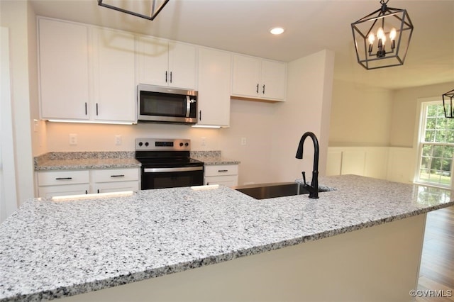 kitchen featuring hardwood / wood-style flooring, sink, white cabinetry, hanging light fixtures, and appliances with stainless steel finishes